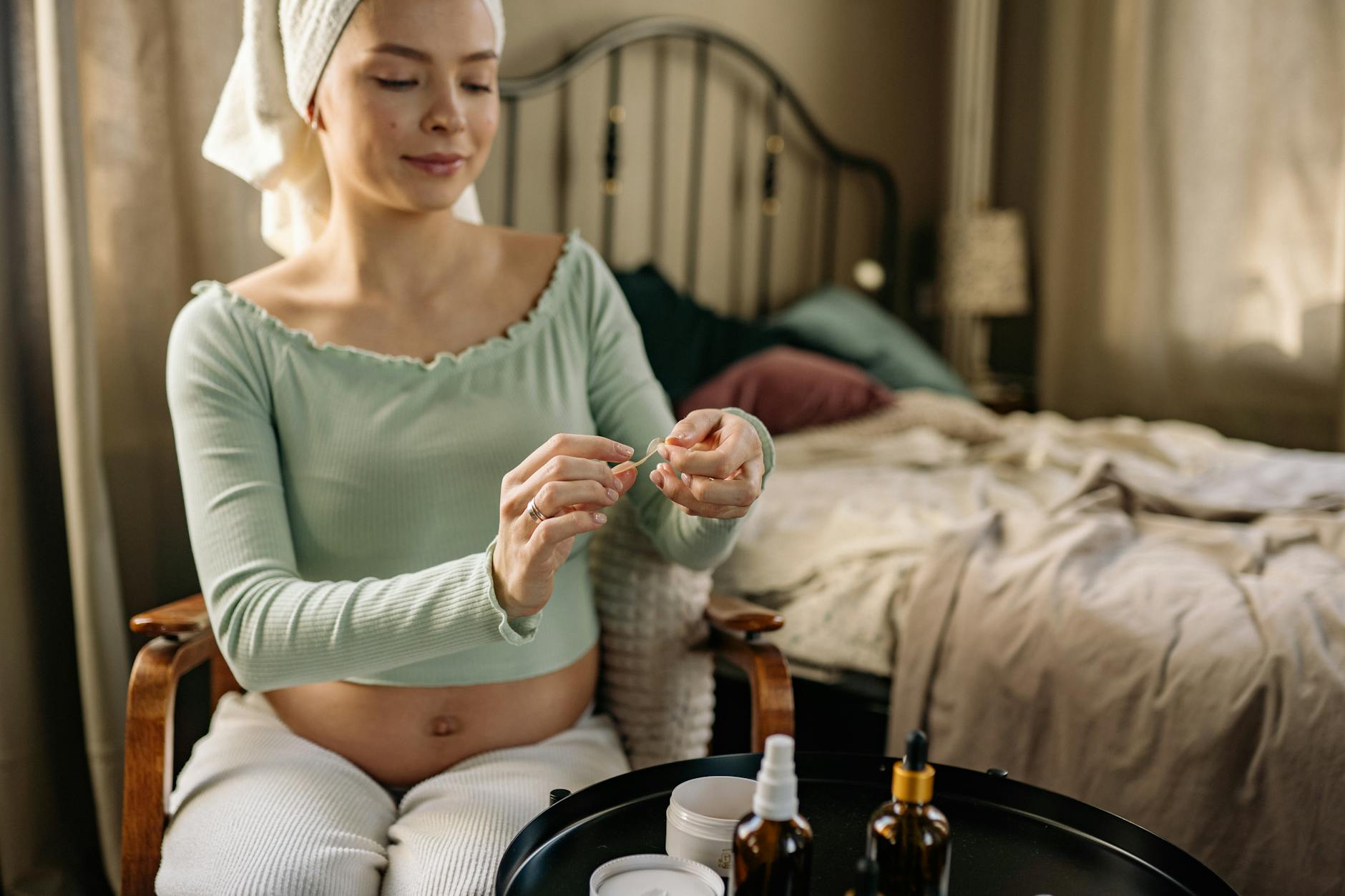 Ciężarna kobieta w domu nakłada naturalny kosmetyk na skórę brzucha