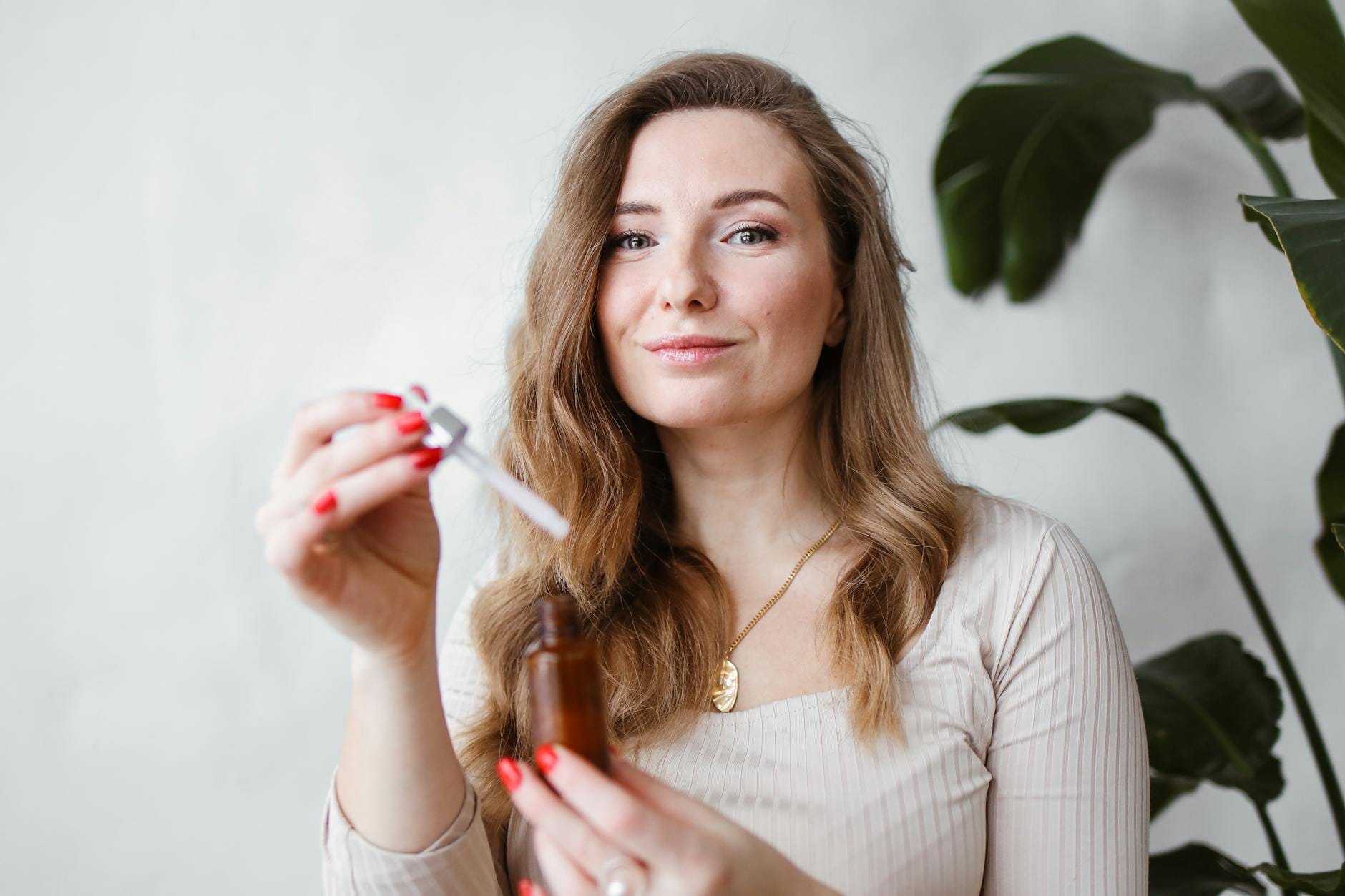 Kobieta nakłada serum pipetą na twarz, obok doniczkowe rośliny