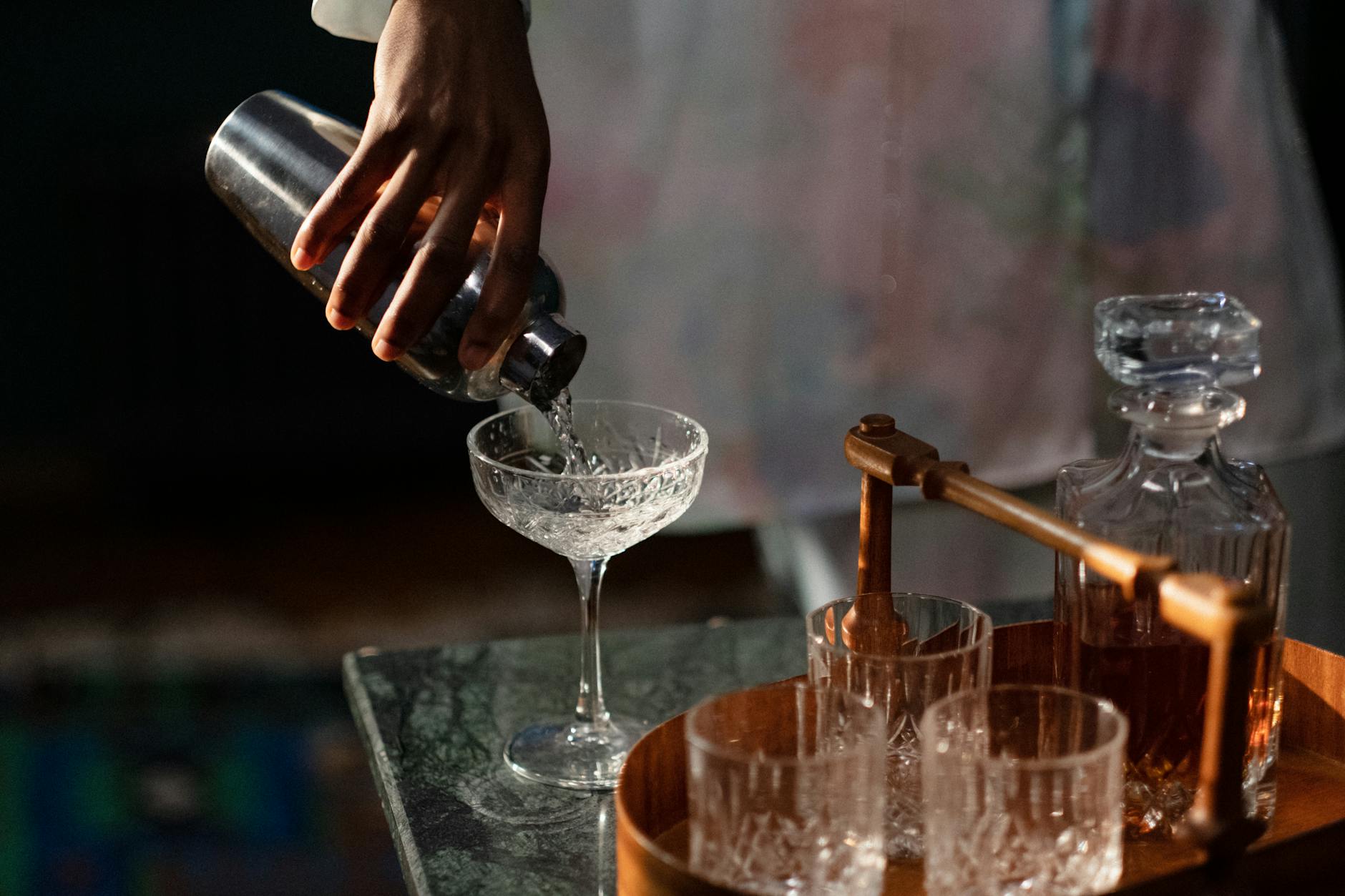 Jak dobrać szkło do alkoholu: przewodnik po kieliszkach i szklankach dla domowego barmana Domowy barman przelewa koktajl z shakera do kieliszka w przytulnym barze