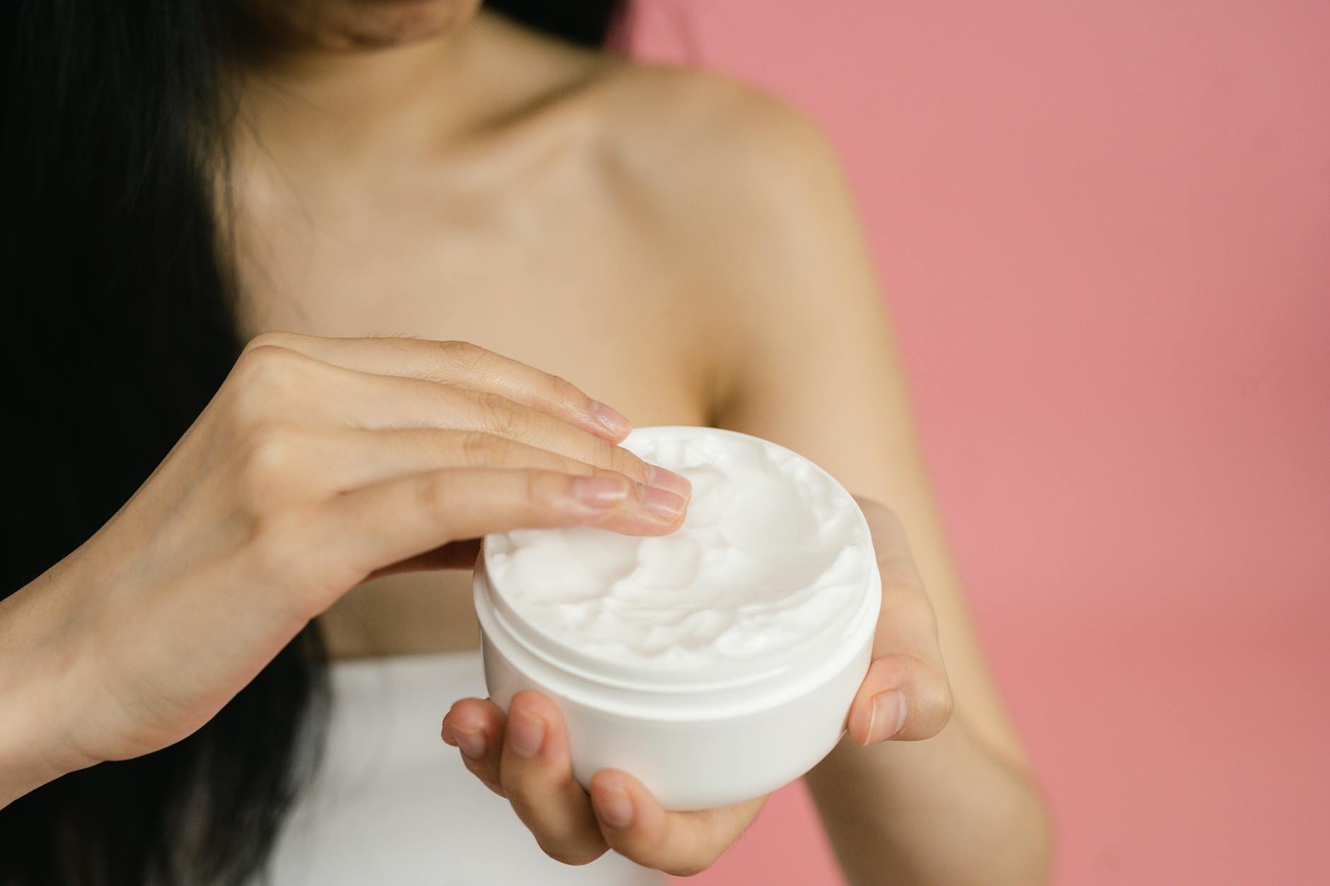 Retinol vs. Kobieta nakłada białą kremową pielęgnację na twarz na różowym tle