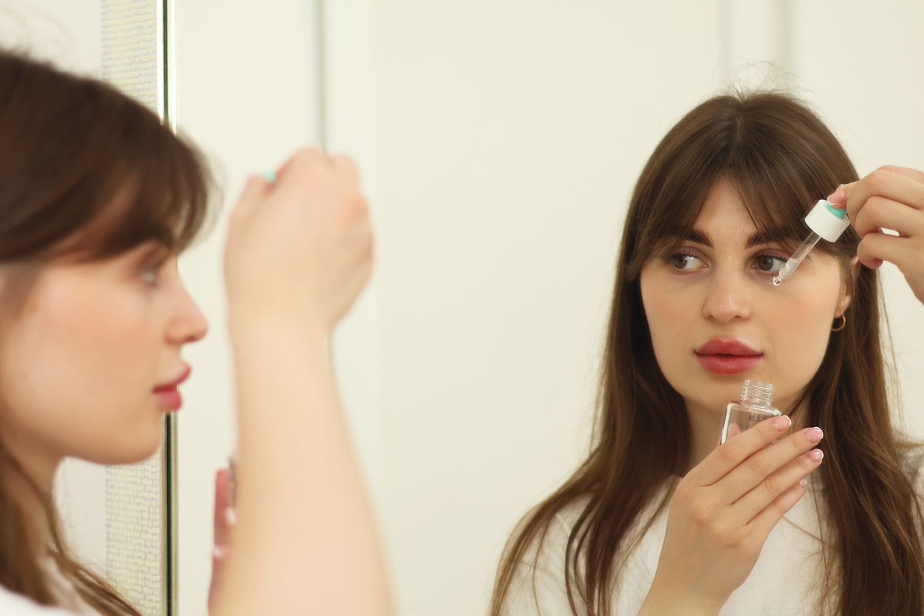 Młoda kobieta nakłada serum do twarzy przy lustrze w łazience